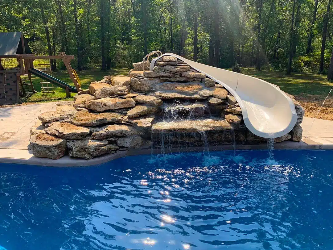 Swimming pool with rock waterfall and slide, clear blue water, and natural stone design in backyard