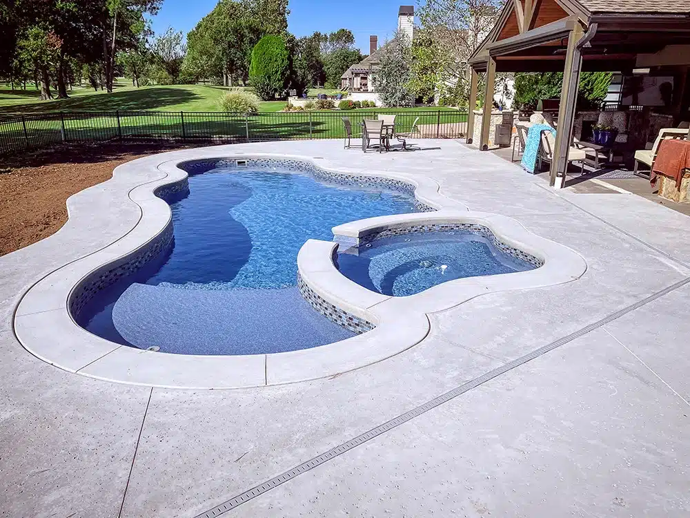 Freeform backyard swimming pool with integrated spa, concrete deck, and outdoor seating area